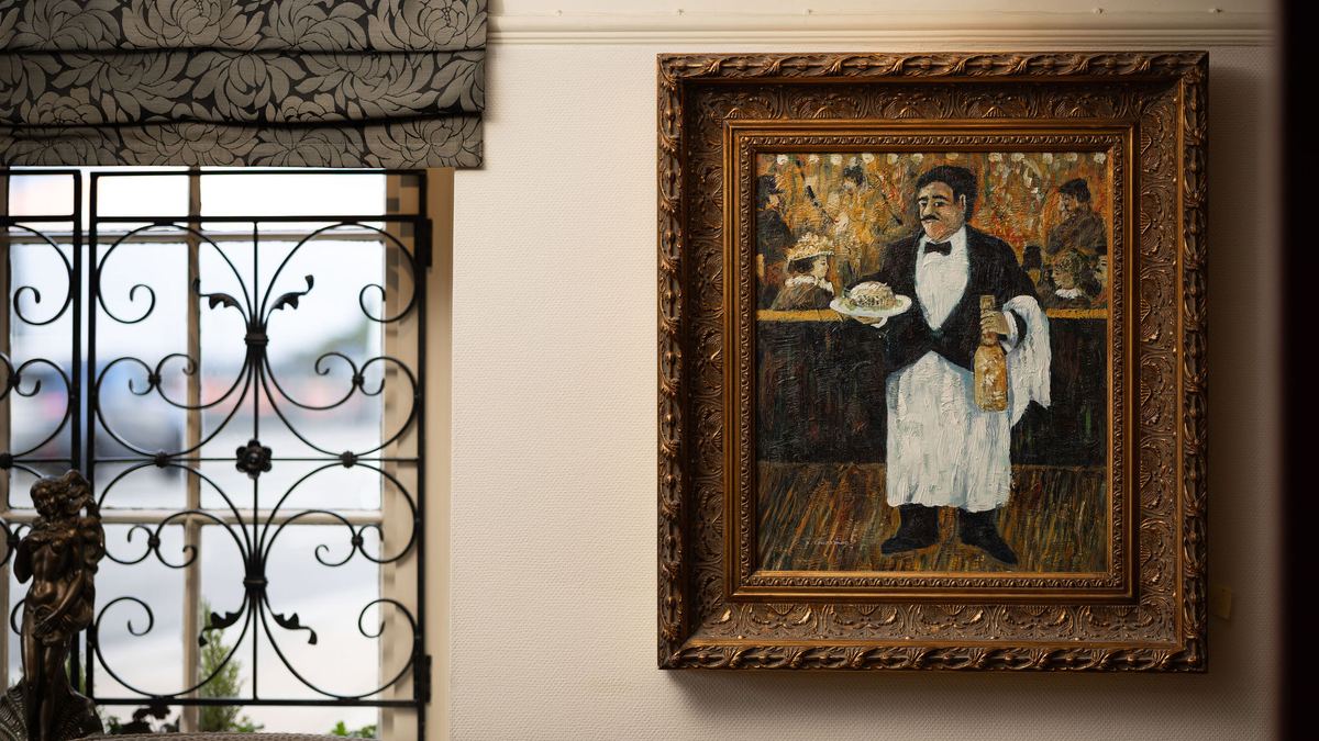 A framed painting of a Parisian-style waiter on the dining room wall at Ennios
